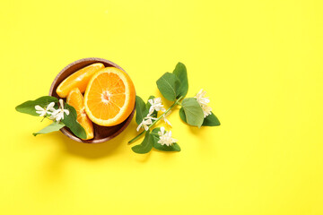 Bowl of oranges with blooming branches on yellow background