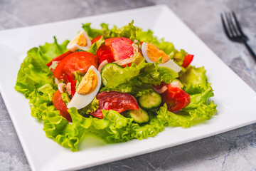 A light vegetable salad for healthy dietary nutrition. Tomatoes, cucumbers and boiled eggs with lettuce and traditional French vinaigrette sauce, on a white plate on a gray table.