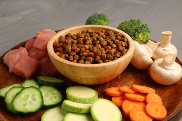 Bowl with dry pet food, raw meat and natural products on table, closeup