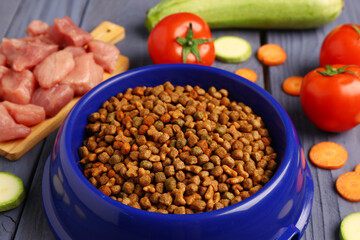 Bowl with dry pet food, raw meat and natural products on color wooden background, closeup