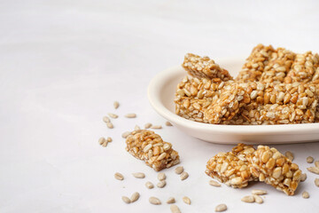 Plate with tasty pieces of kozinaki and sunflower seeds on white background
