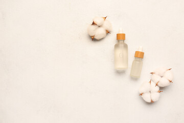 Bottles of essential oil and cotton flowers on light background