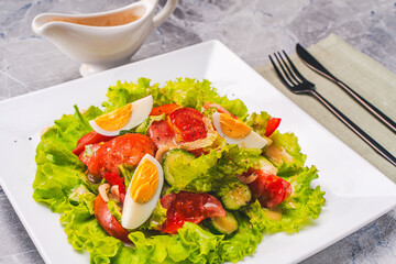 Light vegetable salad with tomatoes, boiled eggs and lettuce, sauce bowl with French vinaigrette sauce and fork with knife on a napkin.