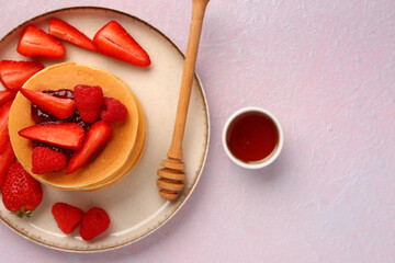 Plate with sweet pancakes, berries and honey on pink background