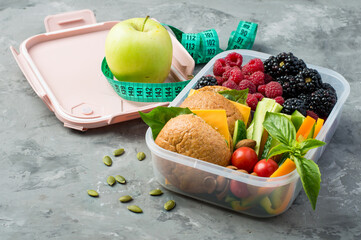 A plastic box with food, a healthy snack to take with you. Sandwiches with cheese, vegetables, berries, apple in a box. Diet, weight control. Horizontal, on a dark background.