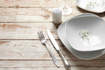 Beautiful table setting with candle and gypsophila flowers on light wooden background, closeup
