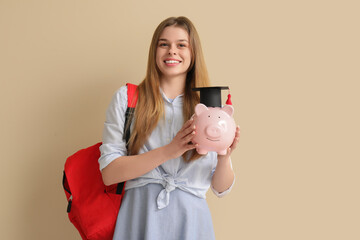 Female student with piggy bank in graduation hat and backpack on beige background. Concept of savings for education