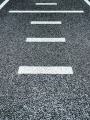 Textured black track or road surface with horizontal dashed lines. Artificial rubber black surface of a running track or road.
