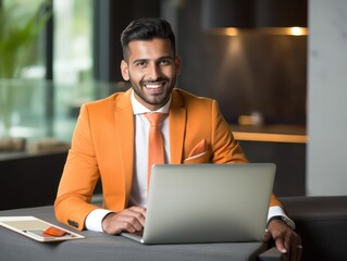 Happy Indian man in orange suit working on laptop