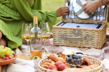 Beautiful young couple with set for romantic picnic and glasses of wine in park, closeup