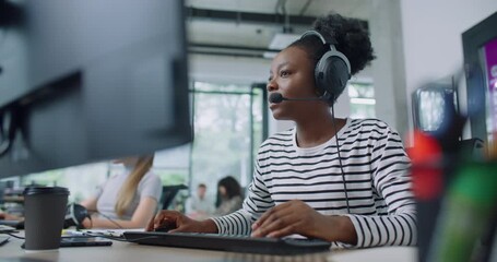 Camera focus on African American woman wearing headset during online consultation with customer. Hardworking manager noting information of conversation on computer. Client service concept. - Powered by Adobe