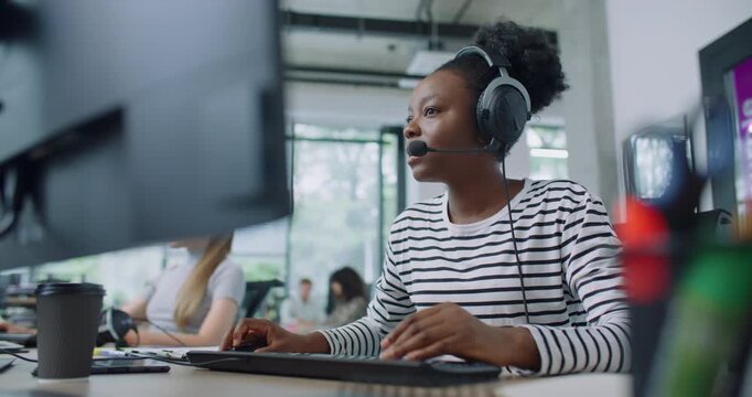 Camera focus on African American woman wearing headset during online consultation with customer. Hardworking manager noting information of conversation on computer. Client service concept.