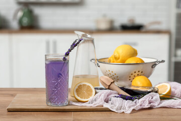 Glass of fresh lavender lemonade with flowers and lemons on table in kitchen