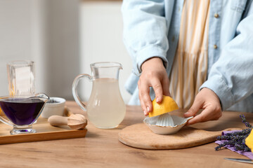 Young woman squeezing lemon in juicer for preparing lavender lemonade at table in kitchen