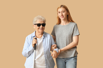 Young woman with blind grandmother on beige background