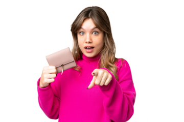 Young girl holding a wallet over isolated chroma key background surprised and pointing front