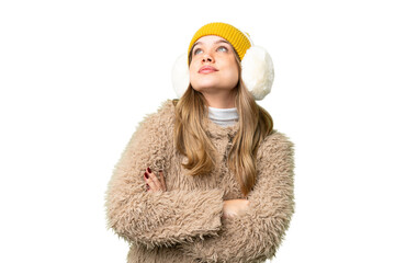 Young girl wearing winter muffs over isolated chroma key background looking up while smiling