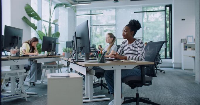 Team of mixed-raced workers sitting at desks and using corporate computers in modern white office. Camera zooming in on beautiful woman typing text on keyboard. Enjoying working in financial company.