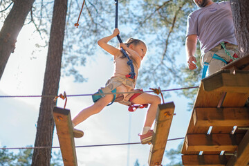 The child walks along the suspended planks of the rope route keeping his balance © Maryna