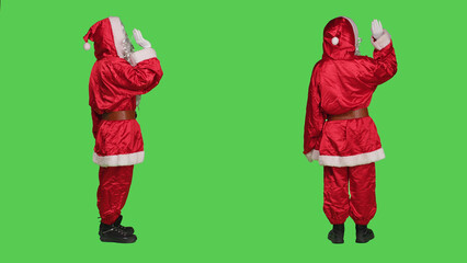 Joyful saint nick greeting people standing over full body greencreen, dressed with festive red suit...