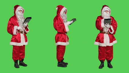 Santa claus using digital tablet in studio, modern cool saint nick working with device during...