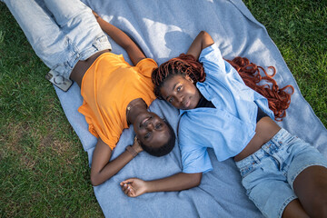 Relaxed carefree african american couple of girls friends lounging, lying on blanket on grass in park. Top view of woman looking at camera. Joy and comfort of their friendship, enjoy leisure time