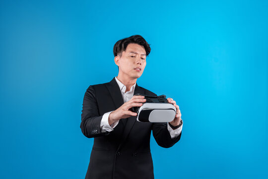 Asian businessman in serious face checking through VR connecting to financial report in futuristic metaverse data analytics communication technology virtual reality at blue copyspace. Contrivance.