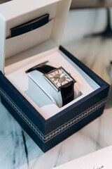 Groom's wedding essentials on table, featuring rings on phone, bow tie, boutonniere, perfume, belt