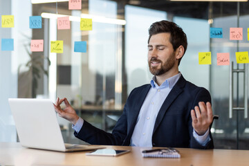 Businessman practicing meditation in office for relaxation and stress relief. Man sitting at desk...