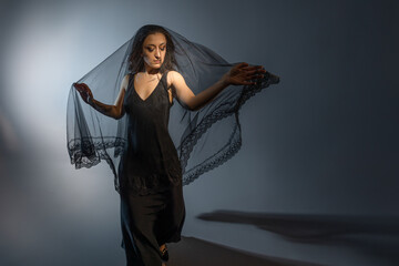A Gothic bride, a mysterious Halloween image, a Gothic gloomy aesthetic. An elegant young woman in a black dress and with a veil on her face