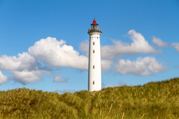 Leuchtturm in den D&uuml;nen vor blauem Himmel mit Wolken