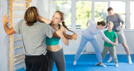 Naklejka premium Man and teen girl at group self-defense lesson are learning new technique of blowing to chin, trainer is practicing technique with other pair in background