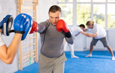 Man works out strength and speed of boxing punch mitts with help of male partner in boxing paws....