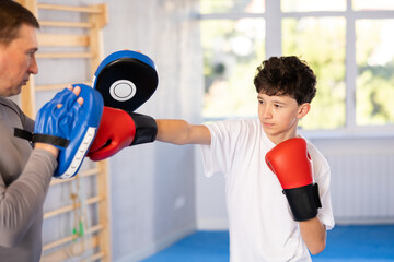 Boy wearing boxing gloves exercise and punch to pads for boxing. Teenage boy with her trainer...