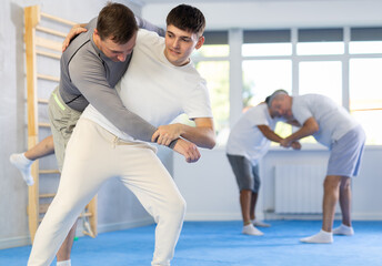 Young guy and man practice wrestling, apply techniques of Aikido and self-defense. Training battle between two opponents in gym during training lesson