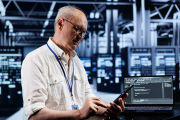 Elderly technician coding in high tech data center using javascript language. Certified specialist updating software on server rigs on laptop terminal, ensuring optimal performance and security