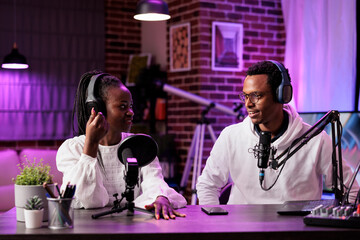 Team of smiling content creators hosting online show in living room studio, filming vlog using professional equipment. Vloggers discussing workflow for upcoming episode for streaming service