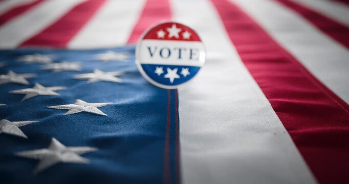 Vote button pin, in the red white and blue of the United States America, pinned to the American flag. To encourage voting, national pride, and political involvement in the US elections. Representing d