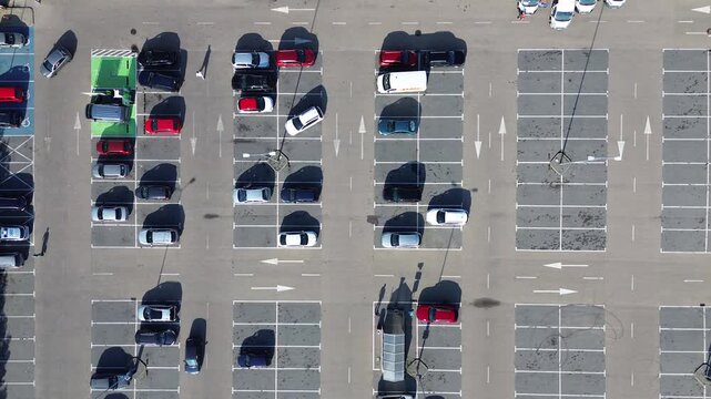 Aerial view of a nearly empty parking lot with scattered vehicles during midday at a suburban shopping center