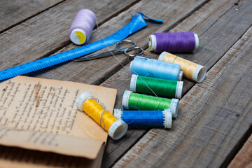 Colorful sewing threads, scissors, measuring tape and an antique book on rustic wood.