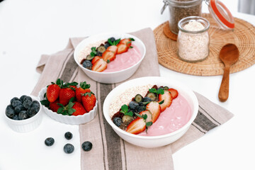 Presented by fruits putting yogurt toppings with strawberry, berry, oats, raisins and chia seed decorated by peppermint in white blow. Pink background. Set of healthy dairy product choice. Pecuniary.