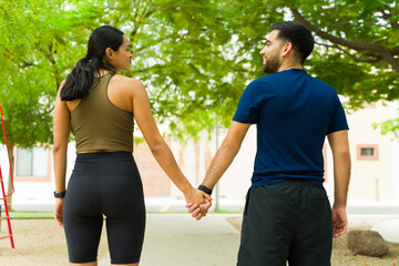 Rear view of a Latin couple in athletic attire happily strolling hand in hand through a park