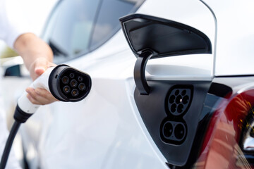 Hand insert EV charger plug into electric vehicle to recharge EV car battery from outdoor charging...