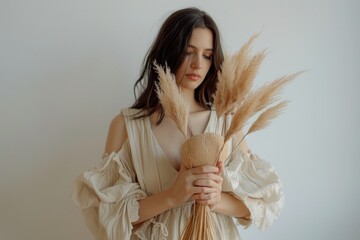 A woman holds a bundle of dried grass, possibly for decoration or craft purposes
