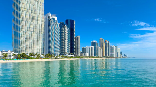 Miami Sunny Isles Beach. Skyscrapers on bright sunny Florida summer day. Ocean with blue clear sky. Travel location for vacation with luxury architecture. City with sand beach and clear blue water.