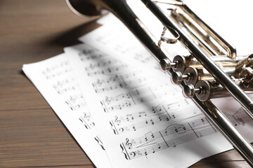 Obraz premium Trumpet and music sheet papers with notes on wooden table, closeup