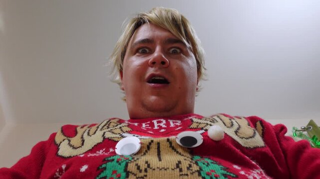 Bottom up inside blond man in ugly sweater comically tears apart holiday paper with fingers, unpacks birthday present, opens mouth enthusiastically wow, surprised by surprise, wish fulfillment, dreams