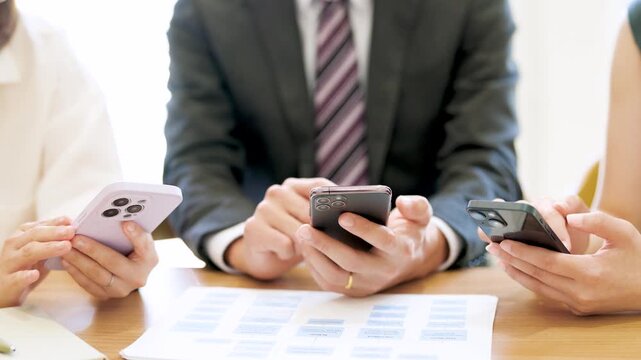 スマートフォンを使って話す男女3人の日本人ビジネスマン