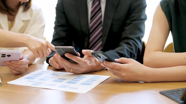 スマートフォンを使って話す男女3人の日本人ビジネスマン