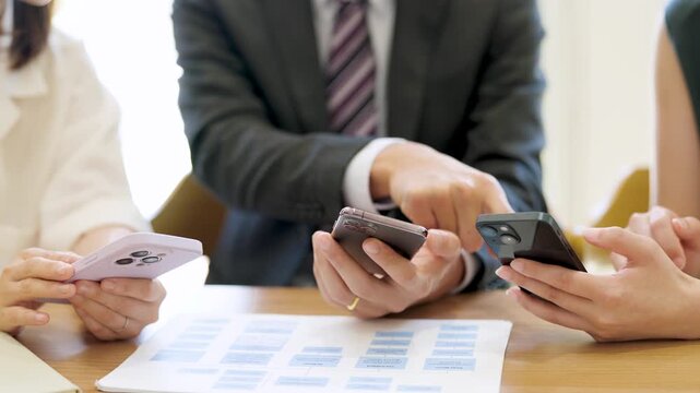 スマートフォンを使って話す男女3人の日本人ビジネスマン